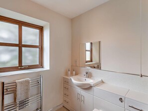 Een badkamer met een raam, een wastafel, een spiegel en een handdoekrek.
