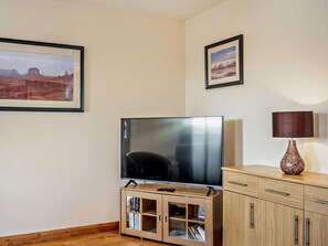 A room with a flat-screen TV on a wooden cabinet, a lamp on a side table, and two framed pictures on the wall. - 3 Bed in Bishop Auckland (oc-94320) (Wolsingham)