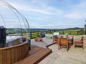 Een overdekt buitengebied met een barbecue, zitplaatsen en uitzicht op het landschap.