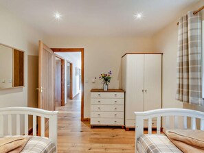 Een slaapkamer met een houten vloer, een wit bed, een garderobe en een dressoir.