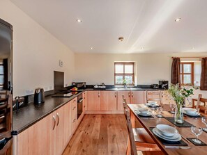 A modern kitchen with wooden cabinets, a black countertop, and a dining area set for four. - 3 Bed in Bishop Auckland (oc-94320) (Wolsingham)
