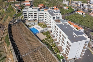 Un hôtel à plusieurs étages doté d’une piscine sur le toit, entouré de jardins en terrasses et d’immeubles d’habitation.
