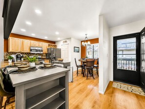Cozinha moderna com armários de madeira, área de jantar com mesa e cadeiras, e uma porta preta com janela.