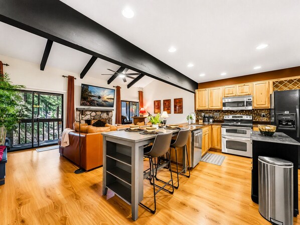 A modern kitchen with wooden cabinets, stainless steel appliances, and a dining area with a bar stool.