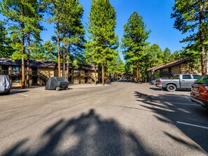 A parking lot with covered vehicles, a building with a balcony, and tall trees. - 2BR mountain condo w fireplace, board games! (Pinetop)