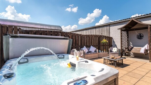 Ein Whirlpool mit Wasserstrahl, eine Holzterrasse, eine überdachte Sitzgelegenheit und eine Backsteinmauer.