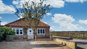 Una casa de una planta de ladrillo con techo de tejas, camino de entrada de grava y valla de madera.
