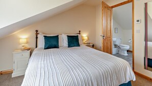 A bedroom with a sloped ceiling, a bed with striped bedding, two bedside lamps, a nightstand, and a wooden door leading to a bathroom. - 1 Bed in Bridgwater (oc-79215) (Ashcott)