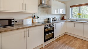A modern kitchen with white cabinets, a stainless steel range hood, a microwave, a toaster, and a window with a view of greenery. - 1 Bed in Bridgwater (oc-79215) (Ashcott)