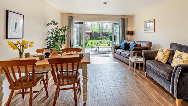 A spacious living area with a dining table, chairs, a sofa, and a view of the garden. - 1 Bed in Bridgwater (oc-79215) (Ashcott)