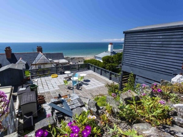 Een dakterras met uitzicht op zee, zitplaatsen buiten en een tuin met rotsen en bloemen.