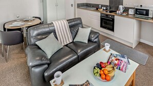 Cocina moderna con microondas, horno y cafetera. Hay un comedor con mesa y sillas, además de un salón con sofá de cuero y una mesa de centro.