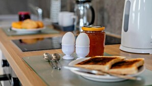 Desayuno con tostadas, huevos, mermelada y una tetera sobre una encimera de cocina.