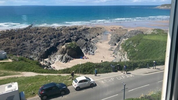 Una carretera costera con una señalización de 'KEEP CLEAR', una playa rocosa y el océano al fondo.
