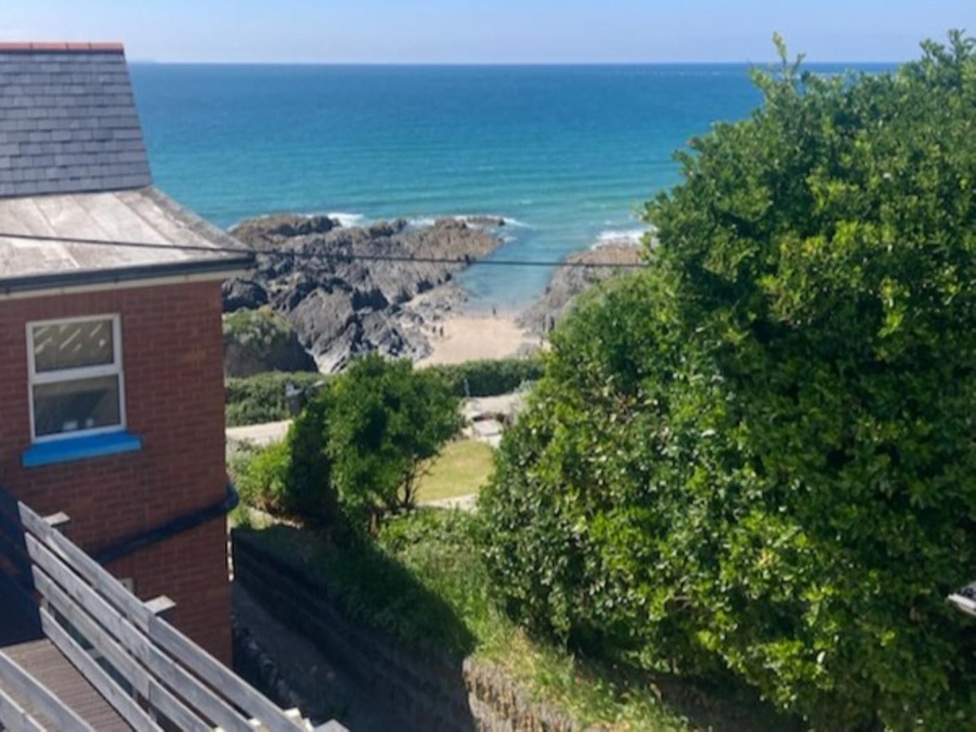A coastal view with a rocky beach, a clear sky, and a building with a sloped roof.