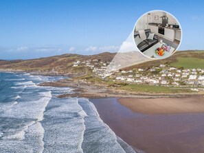 A coastal town with a beach, a view of the sea, and a zoomed-in inset of a modern kitchen with a dining area. - 1 Bed in Woolacombe (oc-76348) (Woolacombe)