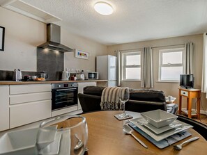 A compact kitchen with modern appliances, a dining area with a table set for two, and a cozy living space with a sofa and a TV. - 1 Bed in Woolacombe (oc-76348) (Woolacombe)