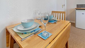 Un tavolo da pranzo apparecchiato con una ciotola blu, un bicchiere da vino e un piatto, con una sedia di legno e un mobile bianco sullo sfondo.