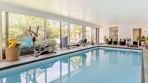 En indendørs swimmingpool med træningsudstyr, store vinduer og et loungeområde.