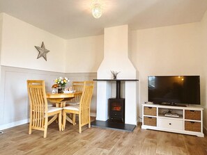 A living room with a fireplace, a dining table with chairs, and a television on a stand. - 2 Bed in Holsworthy (oc-82744) (Pancrasweek)