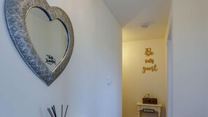 Ein Flur mit einem herzförmigen Spiegel, einem kleinen Beistelltisch mit einem Schild und einem Schild an der Wand mit der Aufschrift 'Be our guest'.