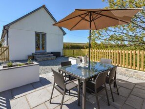 A modern house with a patio area featuring a glass table and wicker chairs, a brown umbrella, and a wooden fence in the background. - 2 Bed in Holsworthy (oc-82744) (Pancrasweek)