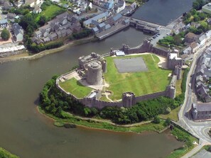 An aerial view of a historic castle surrounded by a moat, with a bridge connecting to a nearby town. - 2 Bed in Pembroke (oc-47640) (Pembroke)