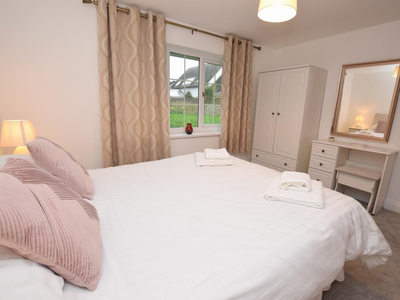 A bedroom with a bed, a dresser, a mirror, and a window with curtains.