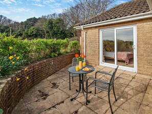 A patio with a table and chairs, a brick wall, and a sliding glass door leading to a bedroom. - 1 Bed in Bembridge (oc-94355) (Bembridge)