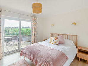 Une chambre à coucher comprenant un lit, une table de chevet, une commode, une fenêtre avec des rideaux et une vue sur l’extérieur.
