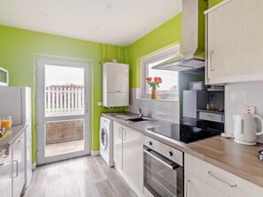 A modern kitchen with a washing machine, oven, and a window with a view of the outside. - 1 Bed in Bembridge (oc-94355) (Bembridge)