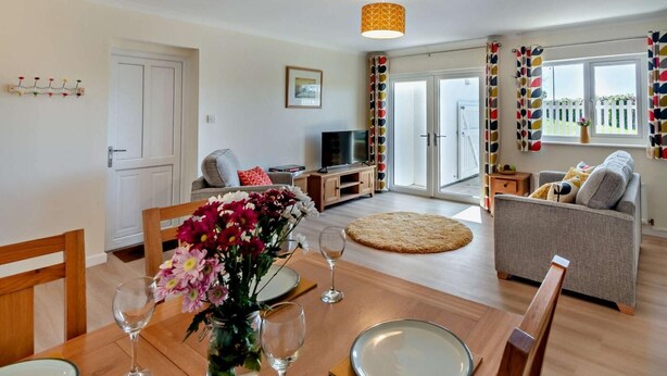 Ein modernes Wohnzimmer mit Esstisch, Sofas, Fernseher und einem großen Fenster mit Vorhängen.