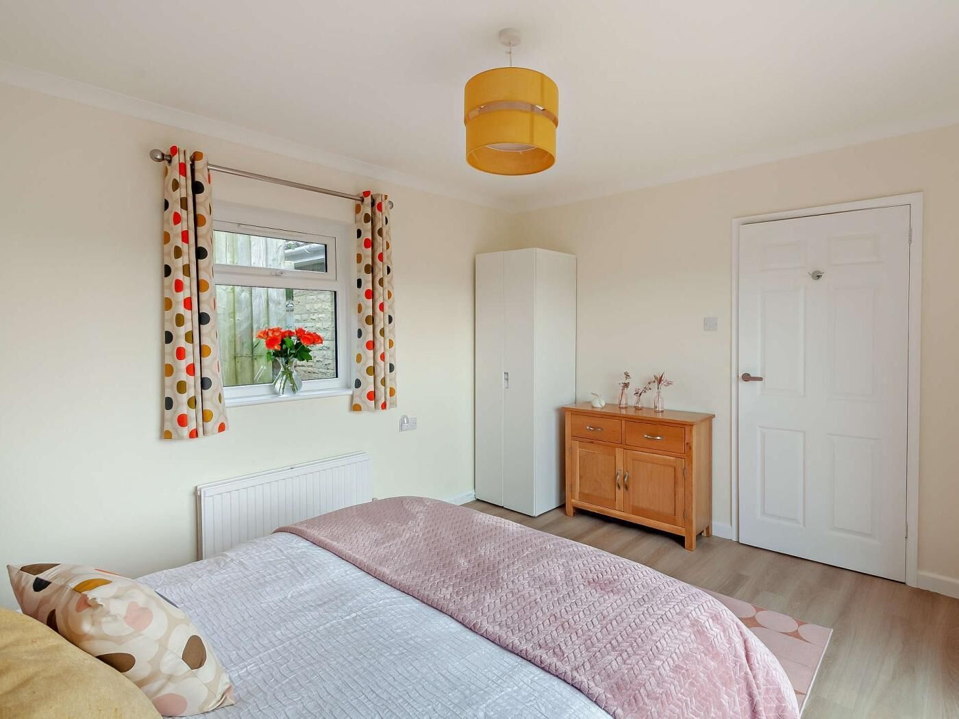 Een slaapkamer met een bed, een kledingkast, een radiator, een raam met gordijnen en een deur.