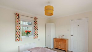 Ein Schlafzimmer mit Bett, Kleiderschrank, Heizkörper, einem Fenster mit Vorhängen und einer Tür.