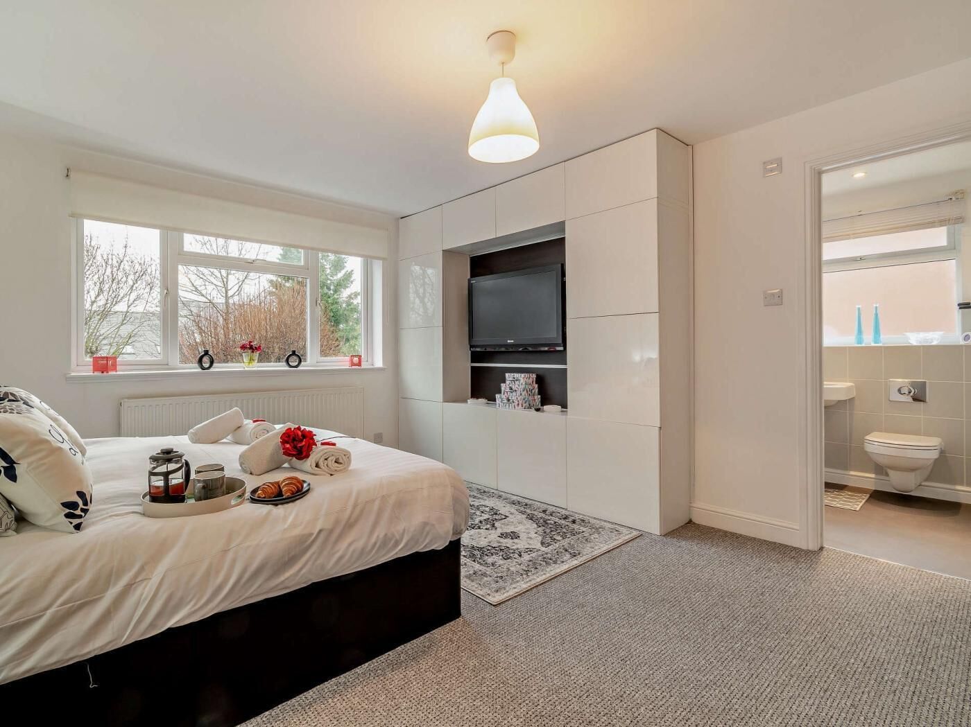 A bedroom with a bed, a TV, a window, and a bathroom.