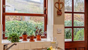 A kitchen with a sink, a window with a view of greenery, and a heart-shaped decoration on the wall.
