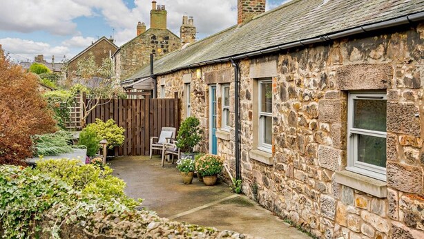 A stone building with a small garden, a wooden fence, and a chair. - 2 Bed in Berwick -upon- Tweed (oc-cn181) (Spittal)