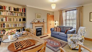 A living room with a fireplace, a bookshelf, a dining table with chess, and a patterned armchair. - 2 Bed in Berwick -upon- Tweed (oc-cn181) (Spittal)