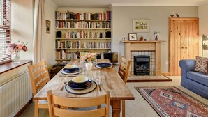 A dining area with a wooden table set for four, surrounded by bookshelves, a fireplace, and a blue sofa. - 2 Bed in Berwick -upon- Tweed (oc-cn181) (Spittal)