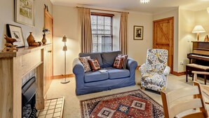A living room with a blue sofa, patterned armchair, fireplace, and a piano. - 2 Bed in Berwick -upon- Tweed (oc-cn181) (Spittal)