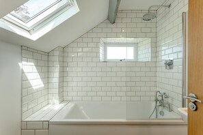 A modern bathroom with a skylight, a bathtub, and a shower area. - 4 Bed in Torrington (oc-78199) (Langtree)