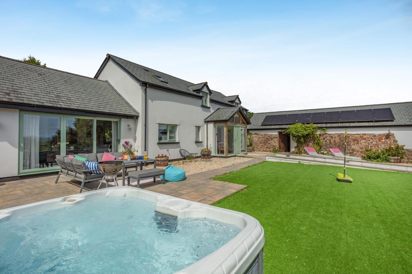 A modern house with a swimming pool, a patio with outdoor furniture, and a well-maintained lawn.