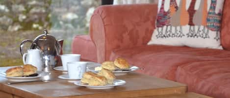 A cozy room with a wooden table set for tea, a sofa with a colorful pillow, and a magazine on the table.