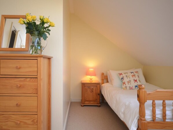 A bedroom with a wooden dresser, a bedside table with a lamp, a bed with patterned pillows, and a mirror above the dresser.
