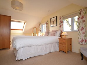 A bedroom with a large bed, a wooden wardrobe, a bedside table with a lamp, and a window with curtains.