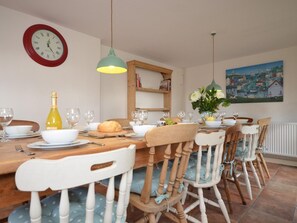 A dining area with a wooden table, chairs, a clock, a painting, and a hanging light fixture.