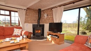 Ein gemütliches Wohnzimmer mit Kamin aus Stein, einem Fernseher auf einem Holzboden, einer Couch und einem Couchtisch mit Frühstücksangeboten.