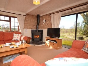 Ein gemütliches Wohnzimmer mit Kamin aus Stein, einem Fernseher auf einem Holzboden, einer Couch und einem Couchtisch mit Frühstücksangeboten.