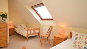 Ein Schlafzimmer mit geneigter Decke, einem Oberlicht, einem Bett, einem Sessel, einem Nachttisch, einer Kommode und einer Lampe.