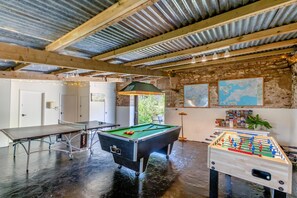 Espaço recreativo interno com mesa de bilhar, mesa de futebol de mesa e mesa de sinuca.